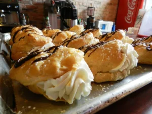 A tray of Apple Walnut filled with whipped cream and topped with a drizzle of chocolate, set against a background with a Coca-Cola machine and coffee equipment.